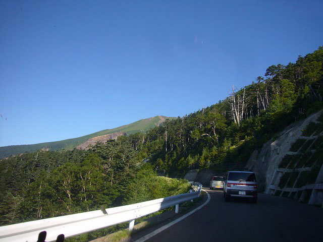 峠道に沿って車を進めると、前方の森の陰から雄大な御嶽山が見えて来ます